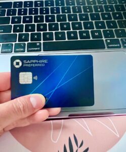 Laptop in background with hand holding a Chase Sapphire Preferred credit card