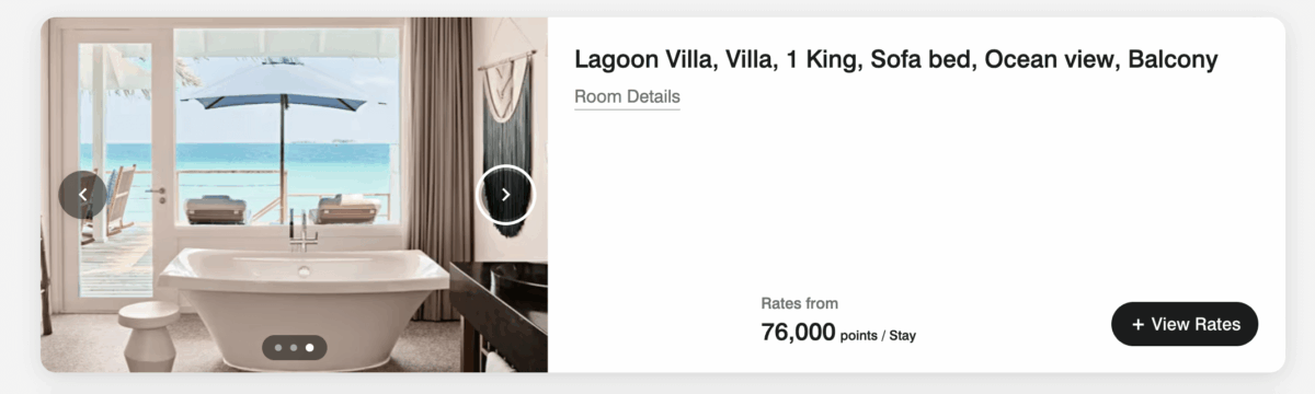 Luxurious hotel room with a white bathtub, ocean view, and balcony. A patio with deck chairs and umbrella overlooks the turquoise water and clear sky.