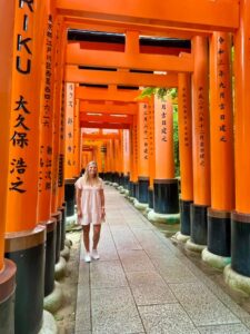 A woman standing in front of a line of orange tori gates.
