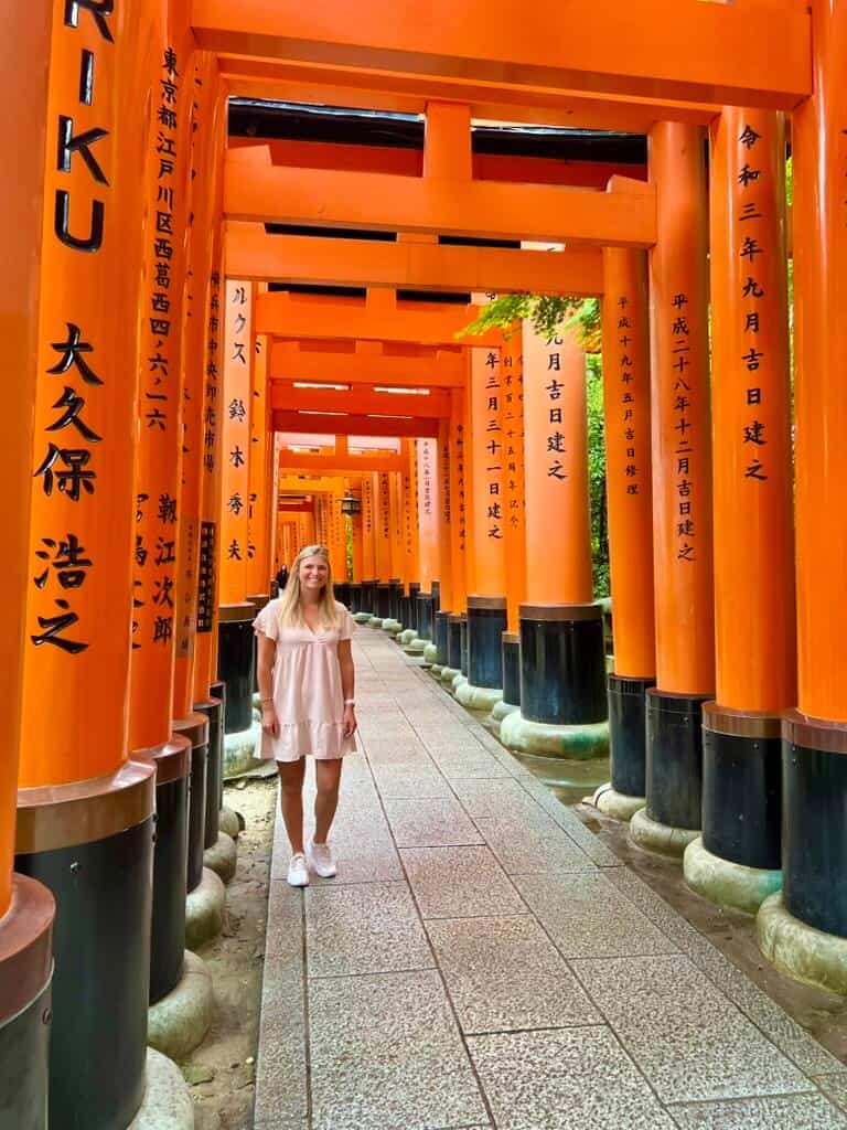 A woman standing in front of a line of orange tori gates.