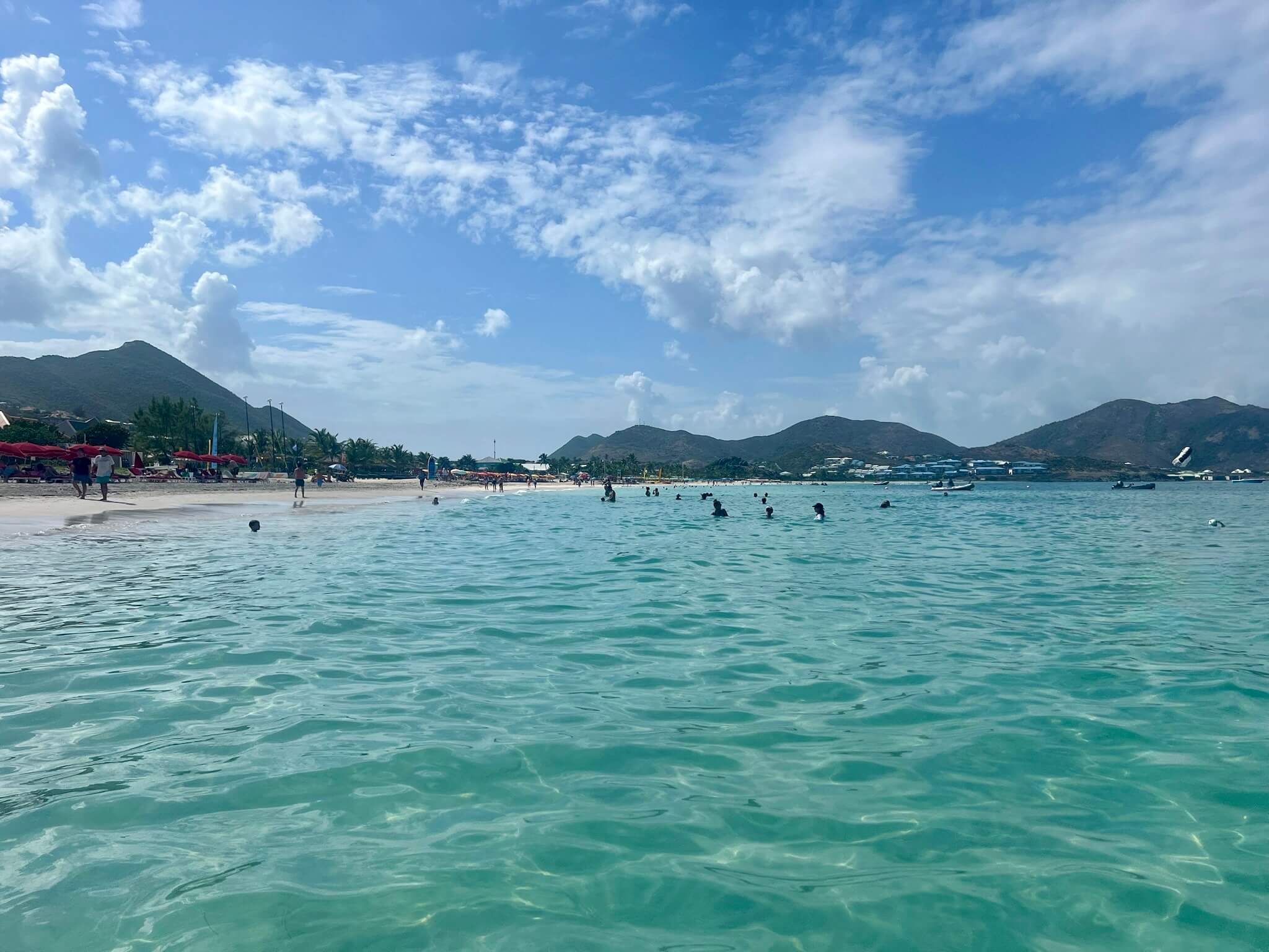 Several individuals are swimming in the ocean at a beach, surrounded by waves and a bright, sunny sky.