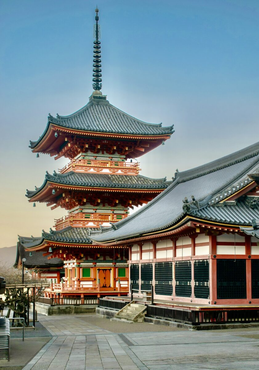 Traditional Japanese pagoda with tiered roofs and ornate details, set against a clear blue sky. The scene is peaceful and architectural.