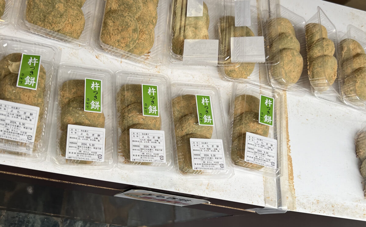 Plastic containers of green, powdered sweets are neatly arranged on a table. Labels with Japanese text are on each pack, suggesting an organized display.