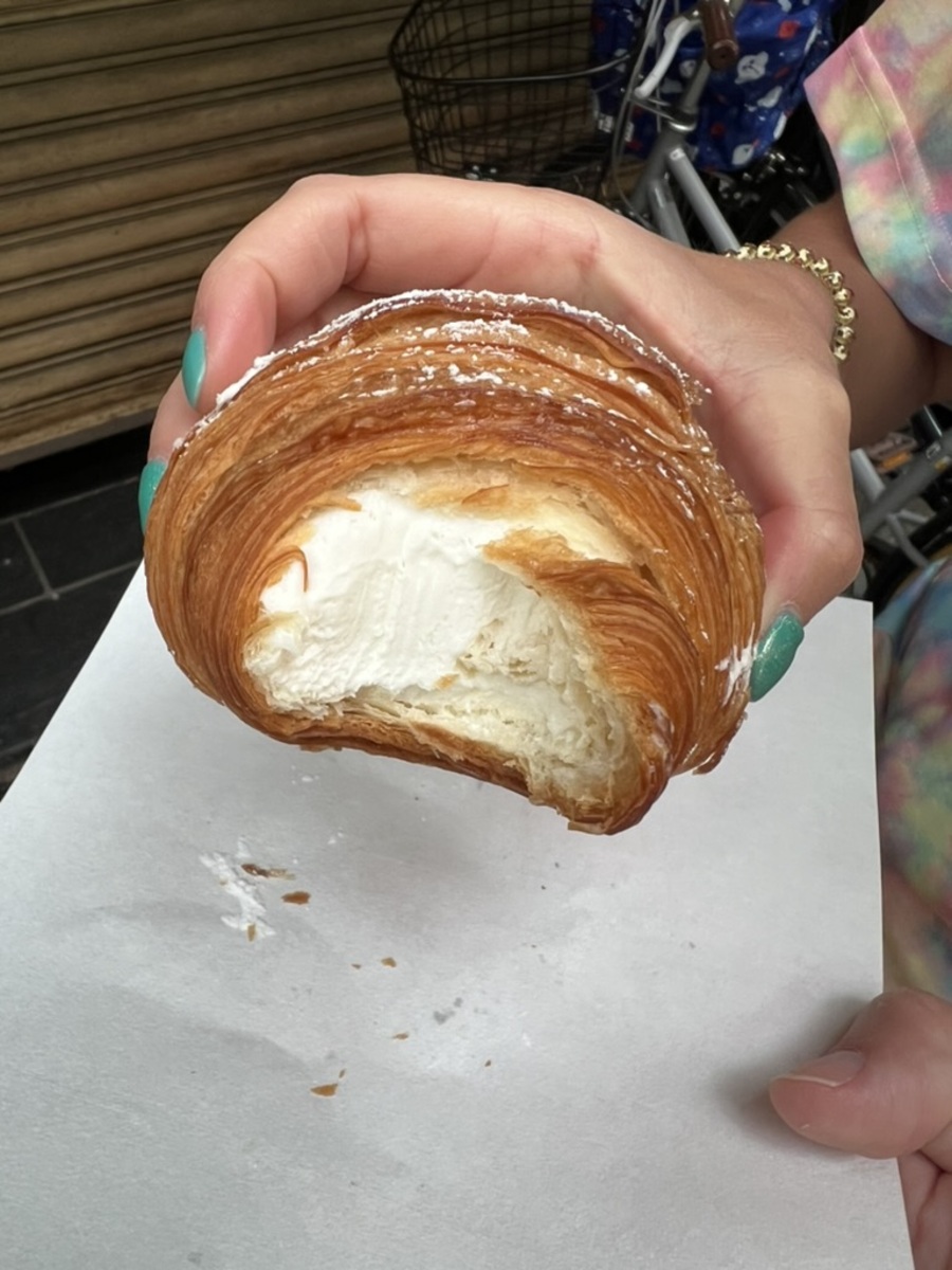 A hand holds a flaky, golden-brown croissant filled with hokkaido creme filling.