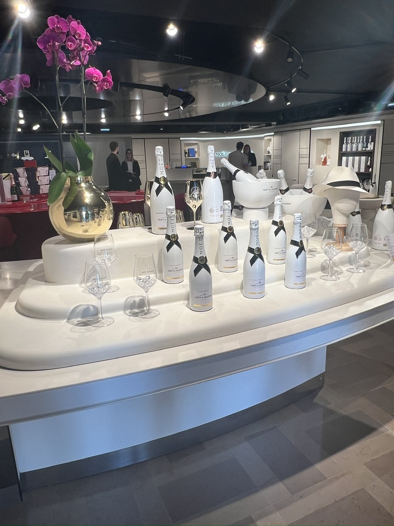 A display with white champagne bottles and empty wine glasses on a modern, curved table. A gold vase with vibrant pink orchids adds elegance.