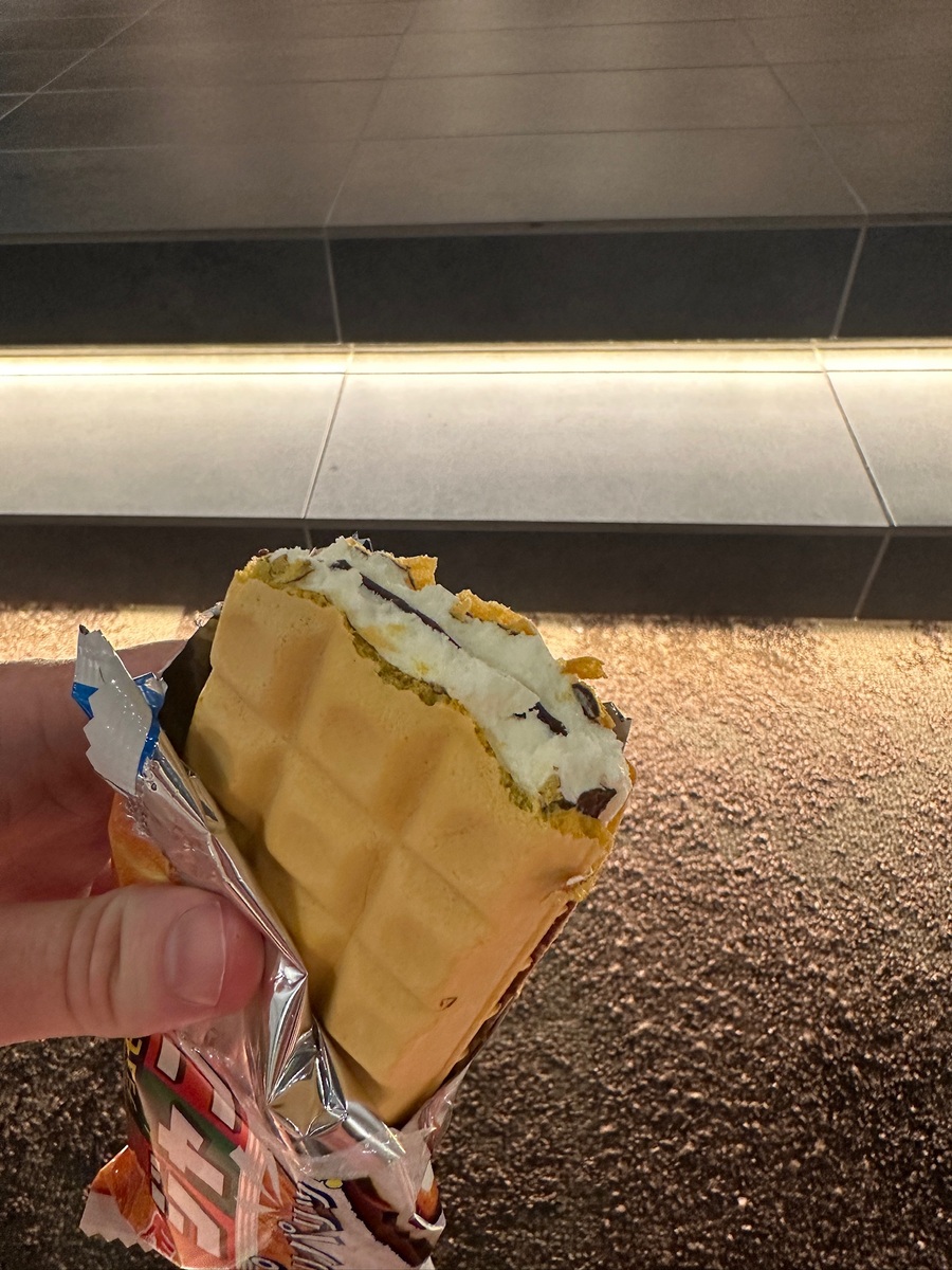 Close-up of a hand holding an unwrapped Morinaga ice cream sandwich with a waffle exterior and chocolate layers.