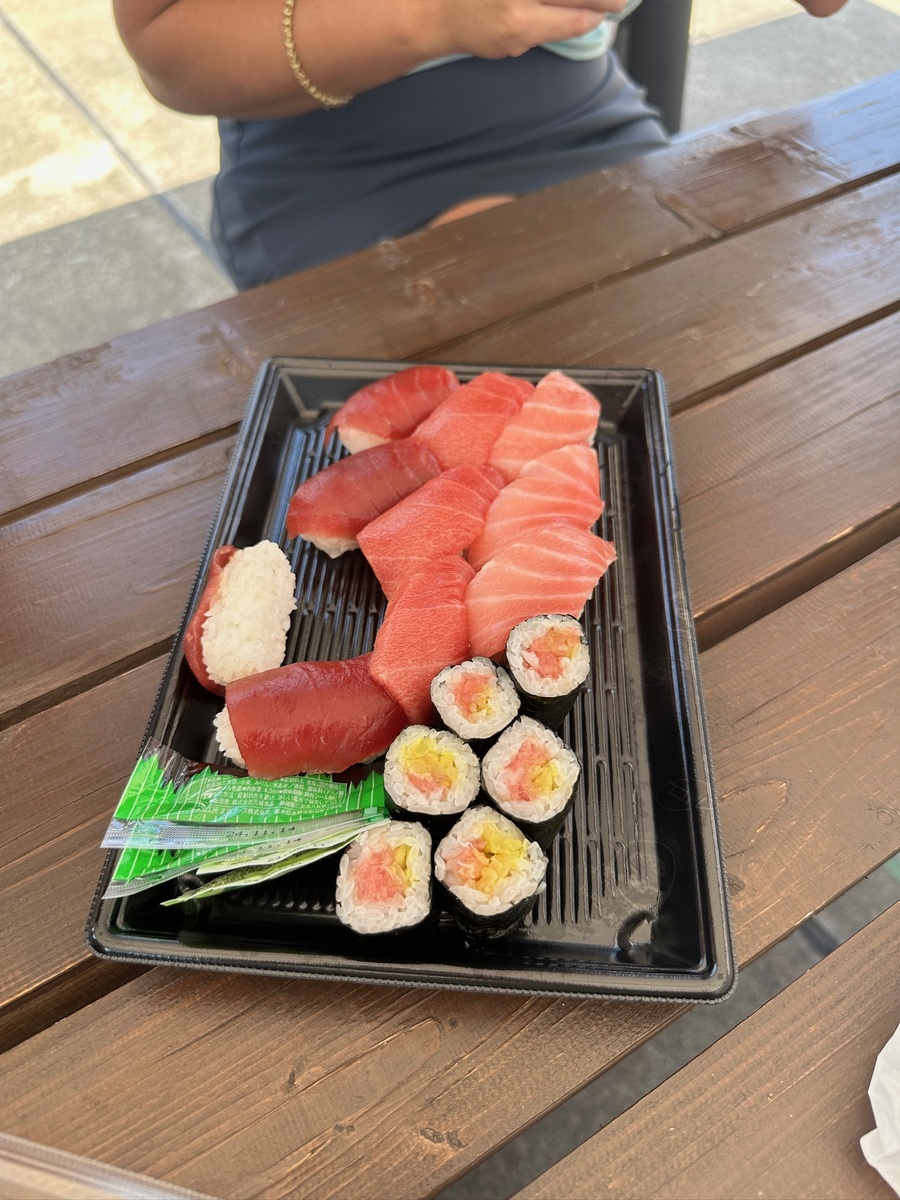 A platter of assorted sushi on a black tray, featuring six nigiri and eight maki rolls with vibrant tuna slices. Placed on a wooden table outdoors.