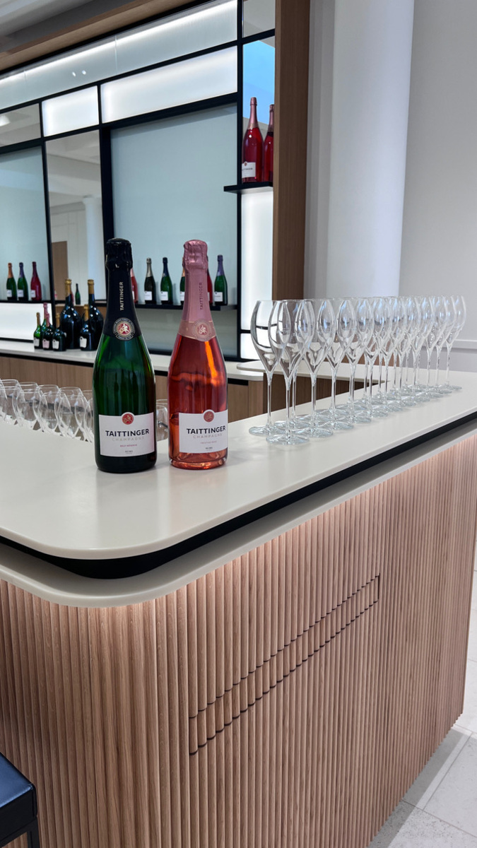 Two bottles of Taittinger champagne, one brut and one rosé, are on a sleek modern bar lined with empty fluted glasses, creating an elegant atmosphere.