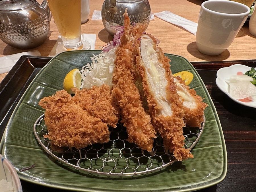 Plate of golden, crispy fried tonkatsu cutlets with shredded cabbage and lemon wedges. Served on a green plate with a metal rack, surrounded by condiments.