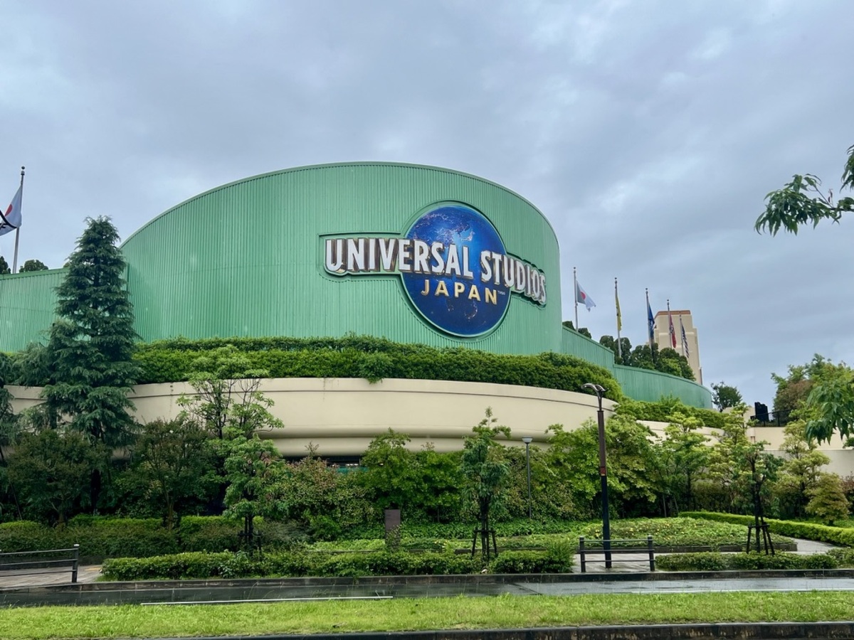 Sign for Universal Studios Japan on a large green building, surrounded by lush greenery. The overcast sky adds a calm, subdued atmosphere.