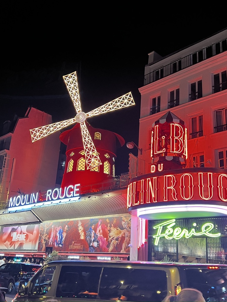 Bright, neon-lit facade of the Moulin Rouge at night, with its iconic red windmill and vibrant signage. Energetic and lively ambiance.