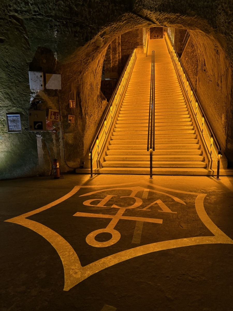 A grand staircase illuminated in warm amber light ascends into rock walls. A large, Veuve Clicquot label adorns the floor, creating a mystical aura.