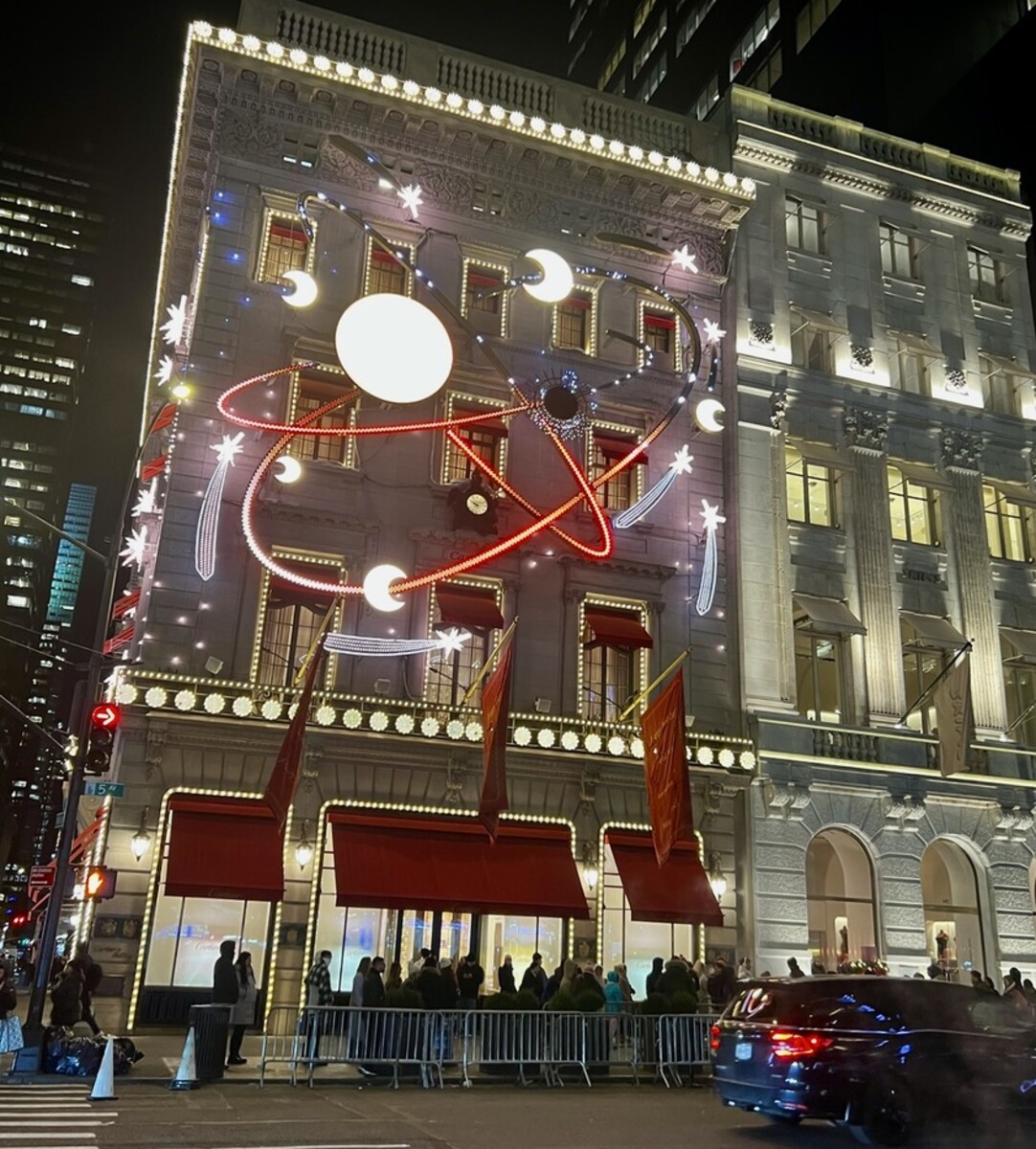 Illuminated building with a celestial theme featuring moons and stars, adorned with red awnings and banners. A crowd gathers near barriers on the sidewalk.