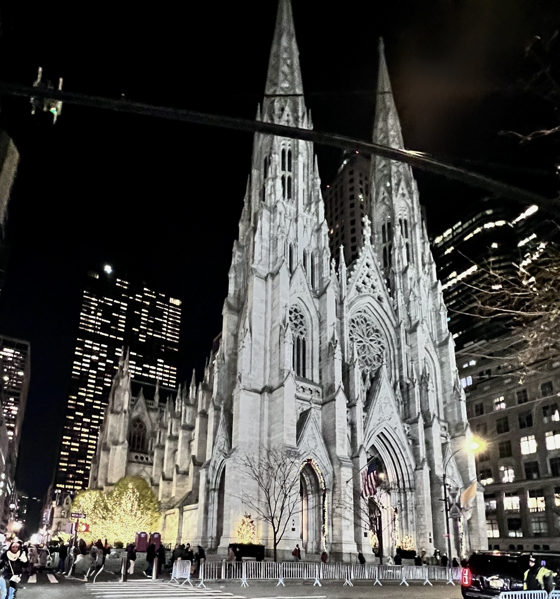 St Patrick's cathedral at night with two pointed spires. The building is illuminated, festive lights and people around create a lively, majestic atmosphere.
