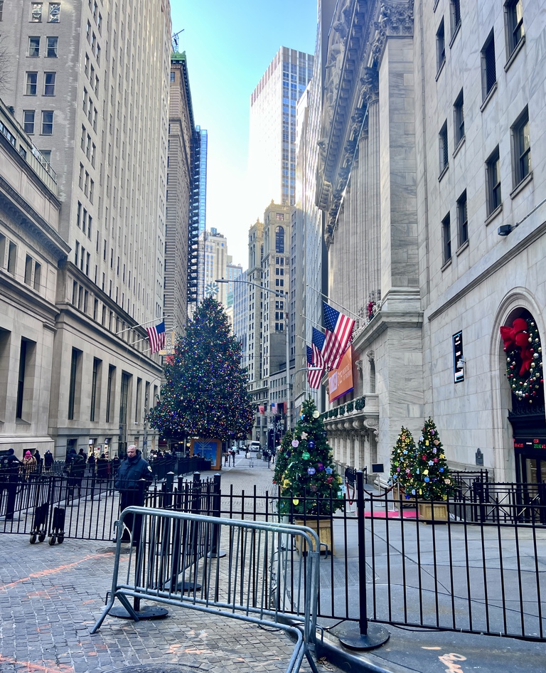 Wall Street scene with tall buildings, Christmas trees adorned with lights and decorations, American flags, and a festive, bright atmosphere.