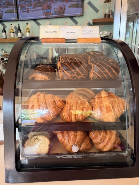 A display case with golden croissants and dark chocolate pastries. Chalk signs label the pastries. Warm, inviting bakery scene with a cozy vibe.
