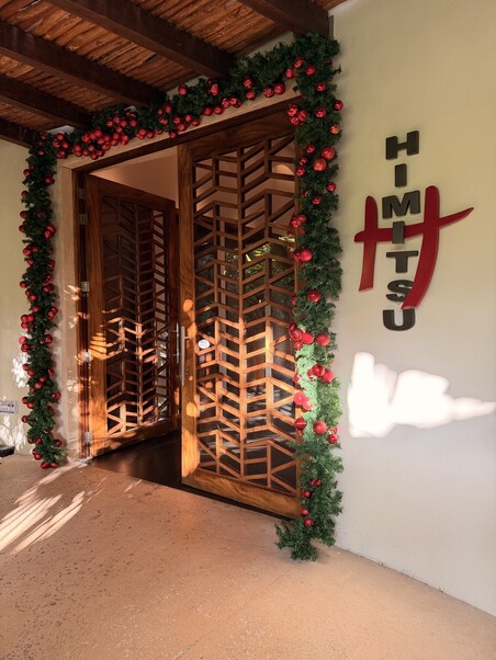 Wooden lattice doors adorned with festive garland and red ornaments create a warm, inviting entrance. The word "Himitsu" decorates the wall in bold, stylish letters.