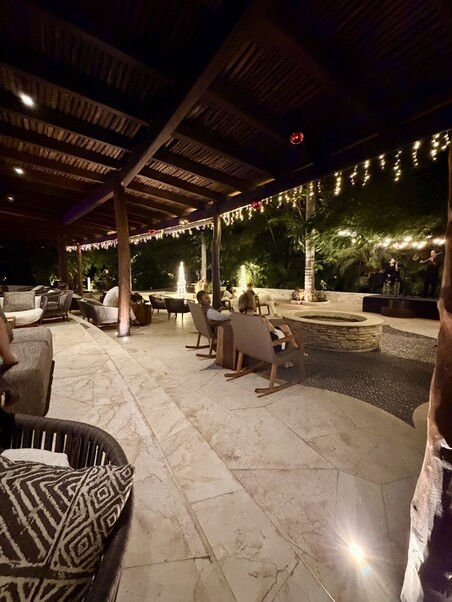 A cozy outdoor patio at night, adorned with string lights under a wooden pergola. Comfortable seating and lush greenery create a tranquil atmosphere.