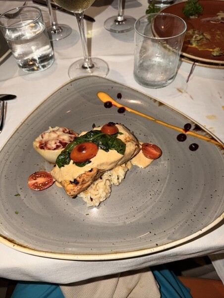 A gourmet dish featuring grilled salmon on rice, topped with tomatoes and spinach on a gray plate. Artful sauce swirls and sides enhance its elegance.