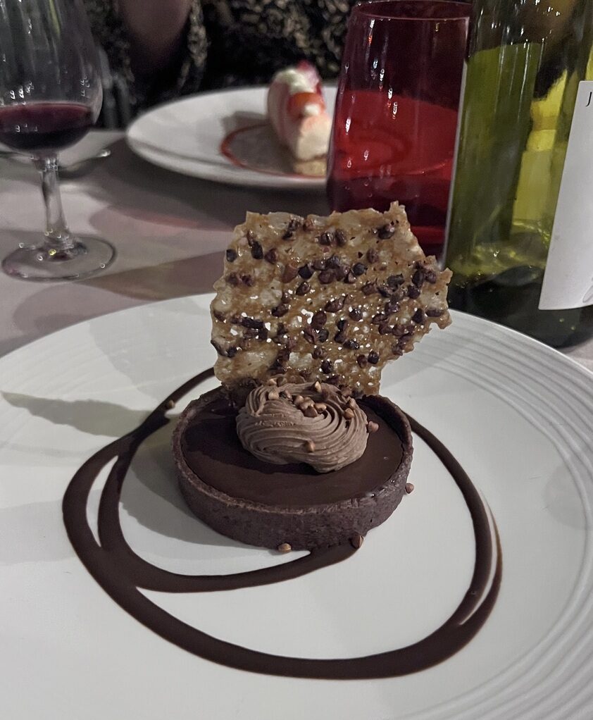 Rich chocolate tart topped with a crunchy nut and caramel crisp, garnished with a swirl of chocolate.