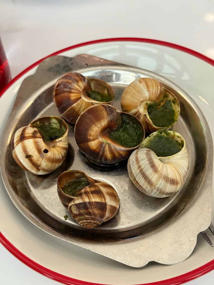 Delicious cooked snails filled with garlic butter served on a metal tray.