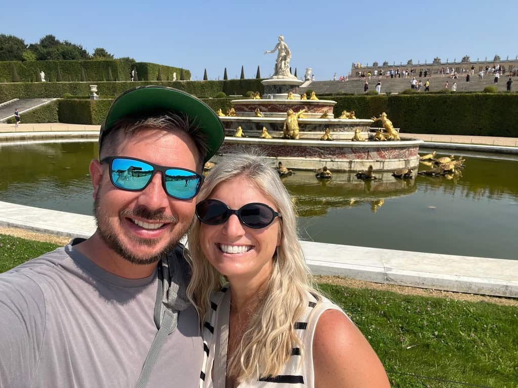 European garden fountain with a smiling couple in sunglasses and casual attire.