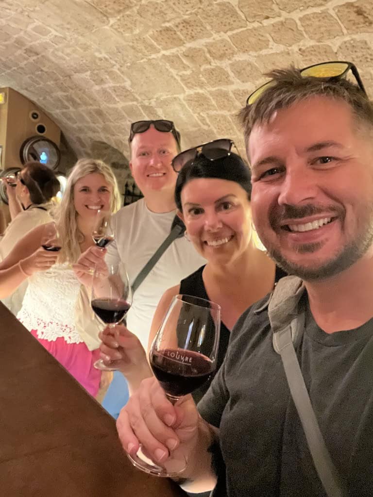 Group of friends enjoying wine tasting together, smiling and holding glasses of red wine.