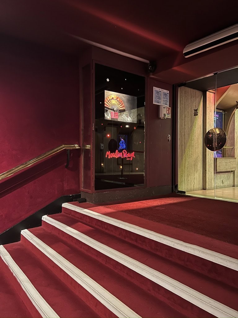 Nightclub entrance with red carpet, stairs, and neon "Moonlight" sign at night.