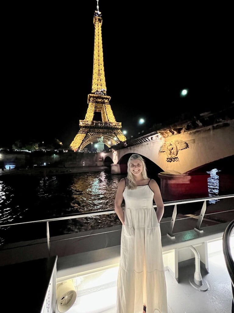 Eiffel Tower illuminated at night with a woman in a white dress on a boat.