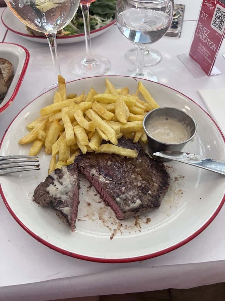 Steak and crispy French fries served with dipping sauce on a white plate.