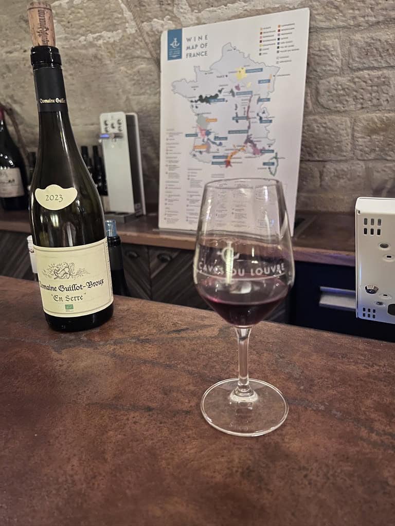 Glass of red wine with winery map and bottles in background.