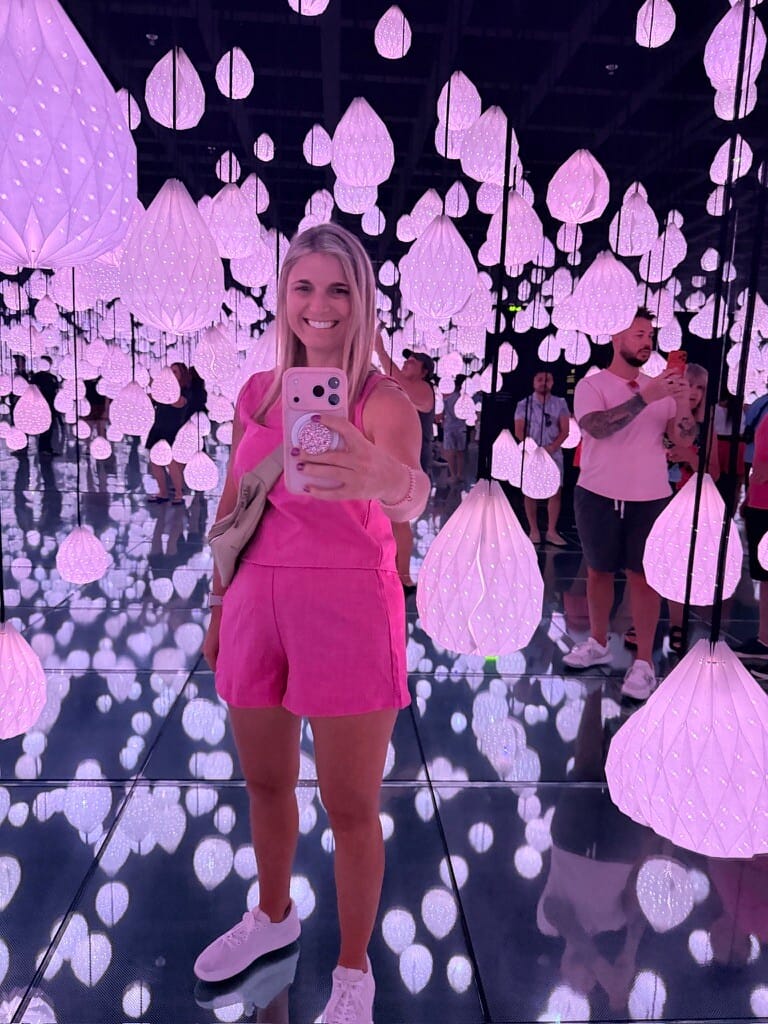 Bright woman taking selfie in vibrant, illuminated art installation with glowing pink and purple han.