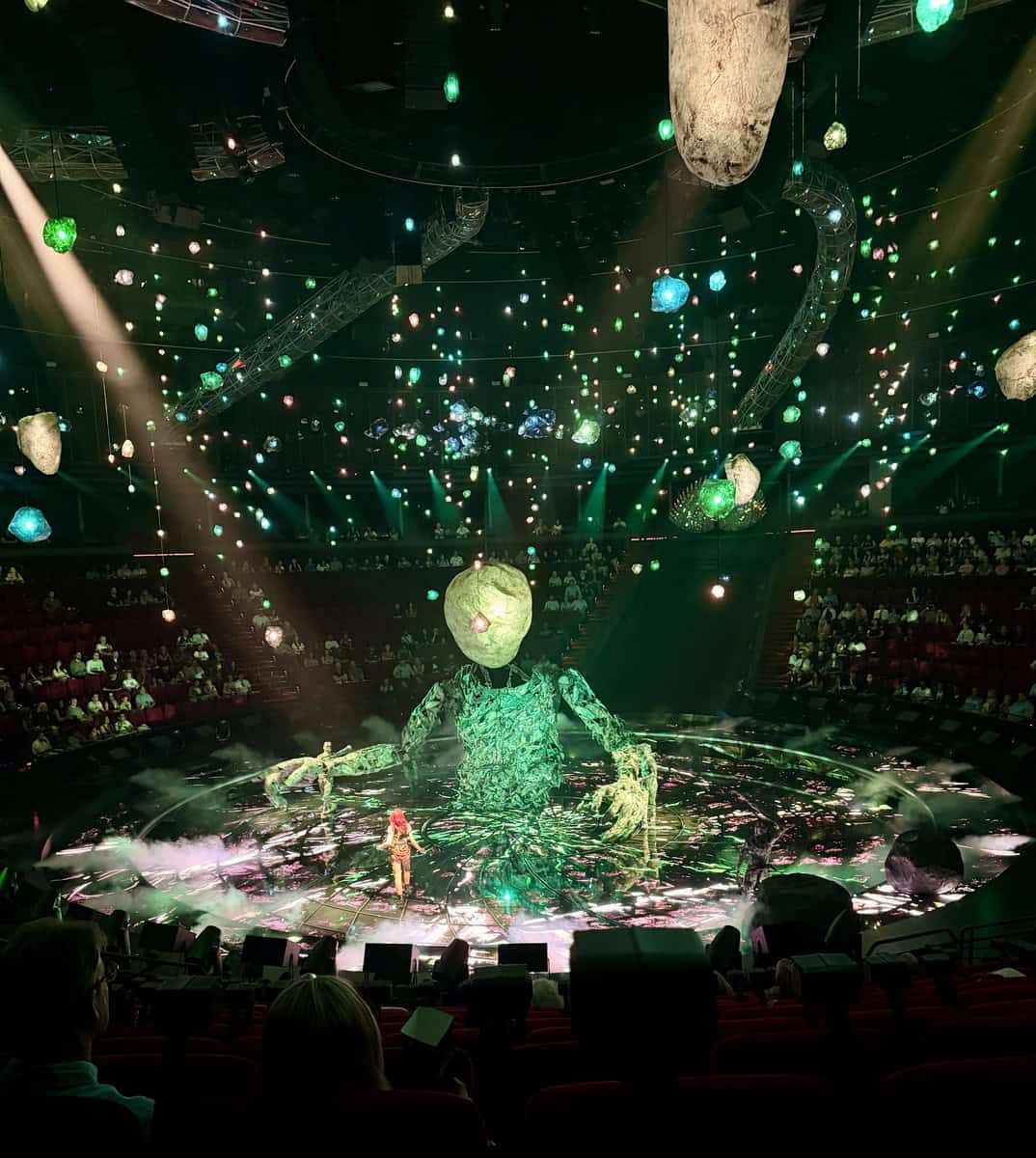 Stunning circus performance with vibrant lighting and giant puppet in a dark arena.