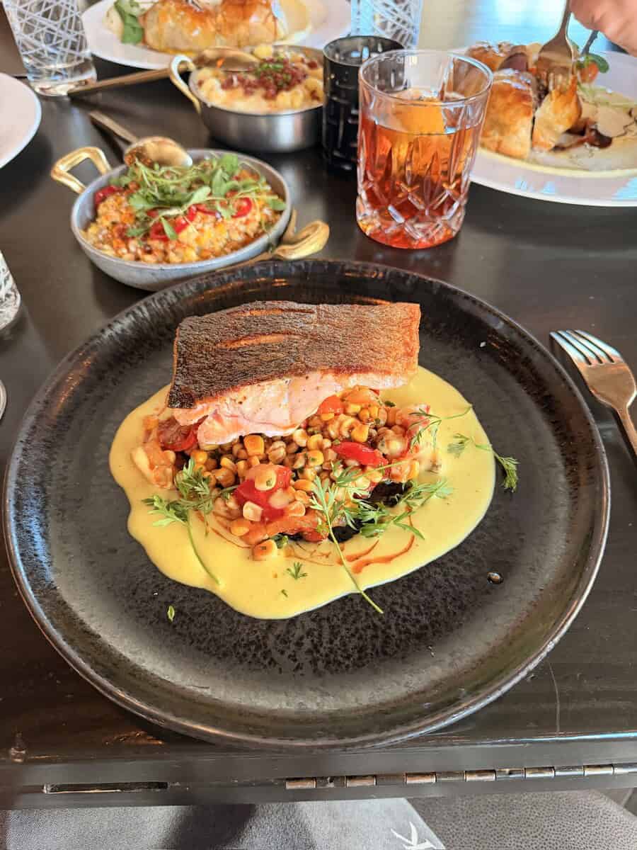 Elegant plated salmon dish with colorful vegetable garnish on a black plate, served with a creamy sa.