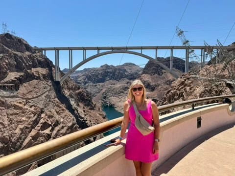 Woman sightseeing at Hoover Dam with bridge and mountains in background.