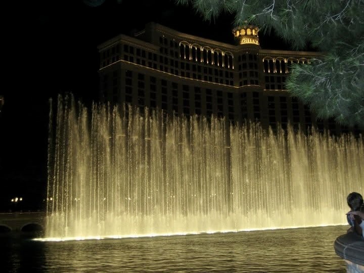 Illuminated fountains at night in front of a grand hotel with arched windows. Warm lights and water jets create a majestic and serene atmosphere.