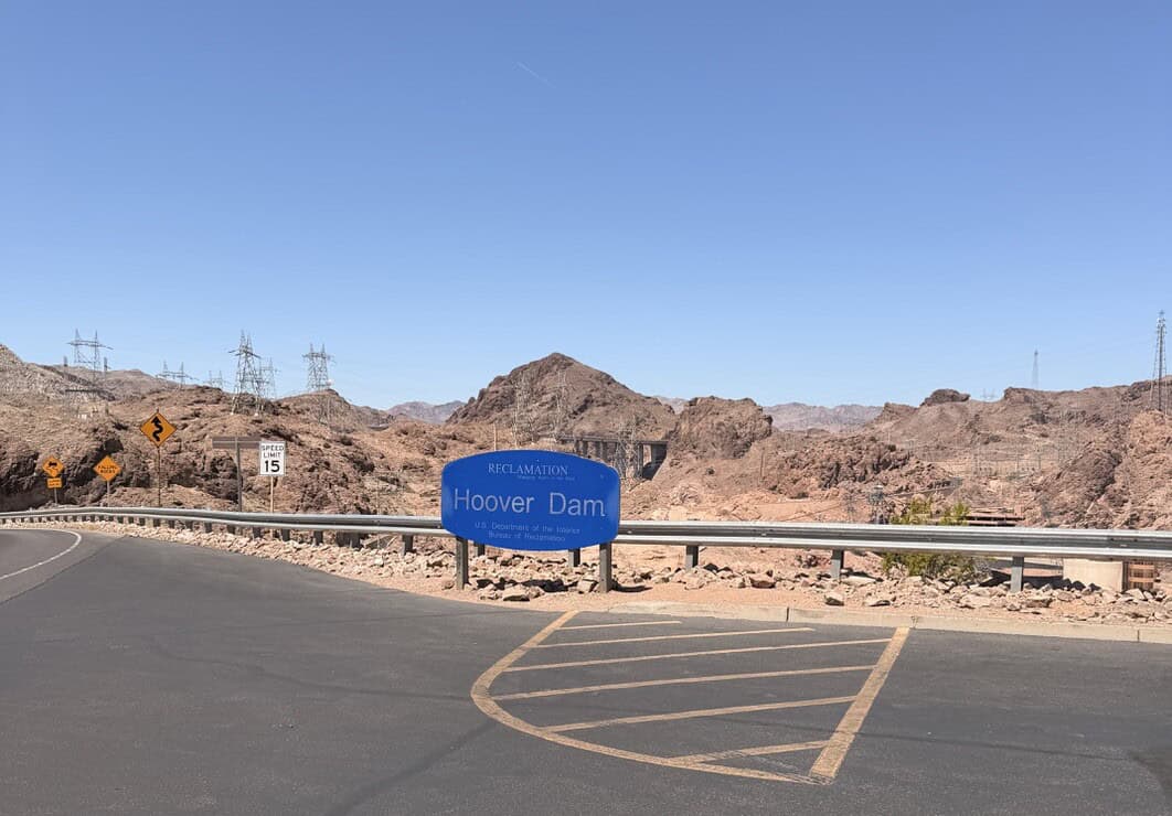 Hoover Dam sign at the roadside with desert landscape in background.