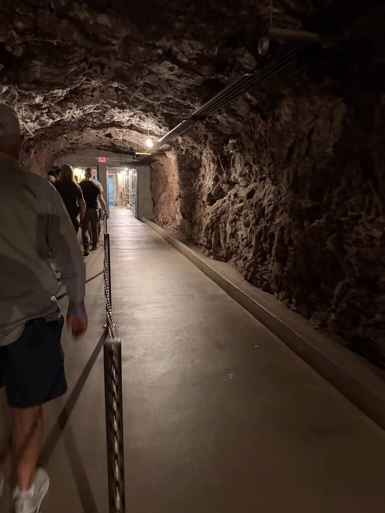 People walking through the Hoover Dam tunnel with rocky walls and lighting.