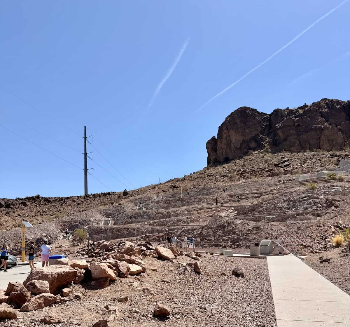 Visitors exploring the Hoover Dam overlook with rocky terrain and clear blue sky.