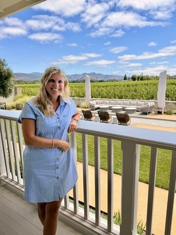 Smiling woman on a balcony overlooking Napa Valley vineyards and mountains.