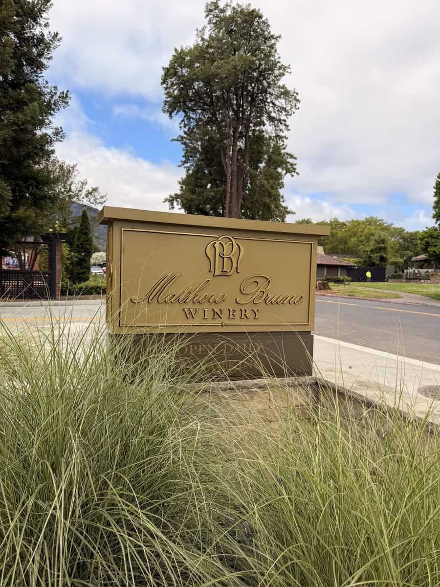 Mathew Bruce Winery sign at Napa Valley vineyard with trees and blue sky.