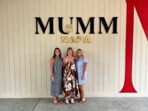 Three women standing in front of Mumm Napa sign at winery.
