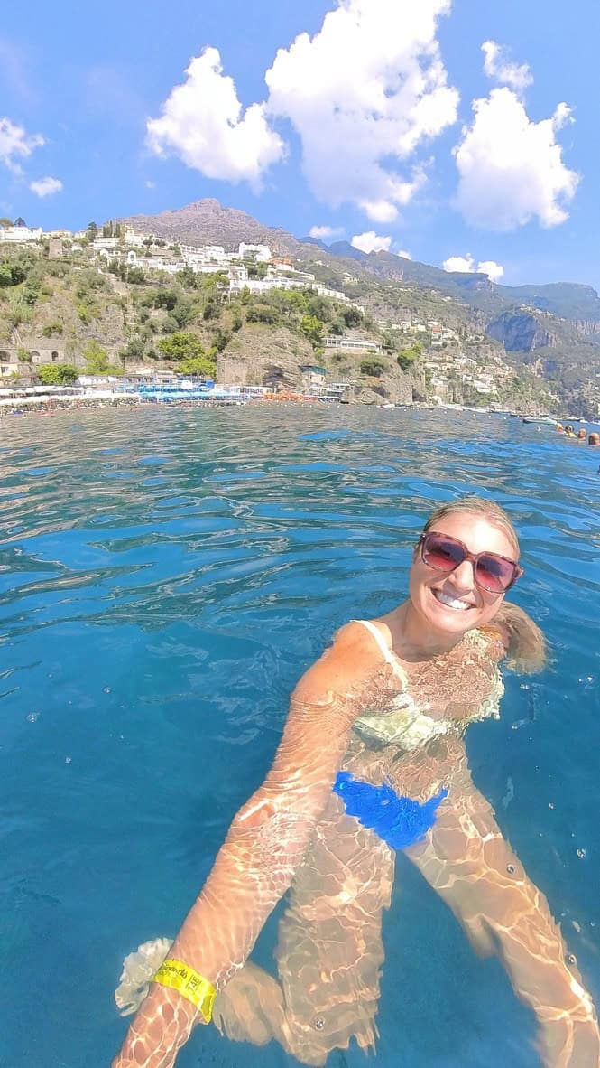 Woman swimming in blue waters with scenic Amalfi Coast in background.
