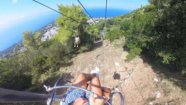 Scenic view from a cable car ride over lush green hills and the sea in Italy.