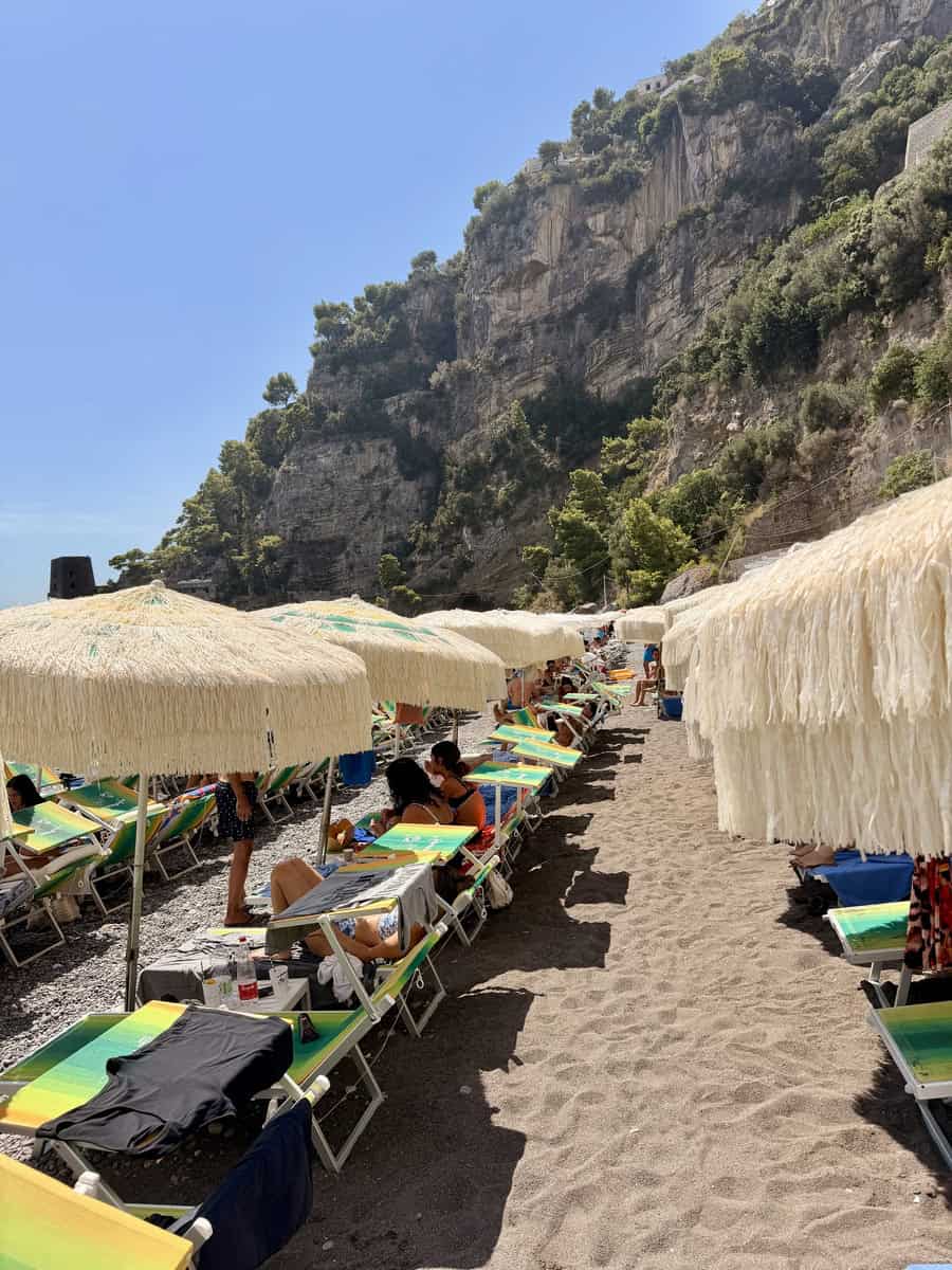 Beach with umbrellas and lounge chairs along a rocky coastline under a clear blue sky.