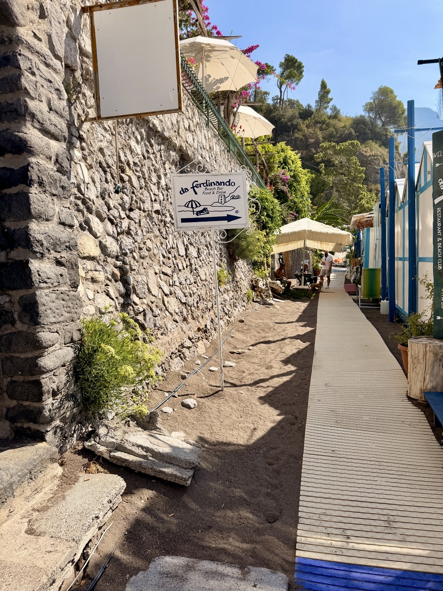 Charming seaside walkway with stone wall and colorful umbrellas in Italy.