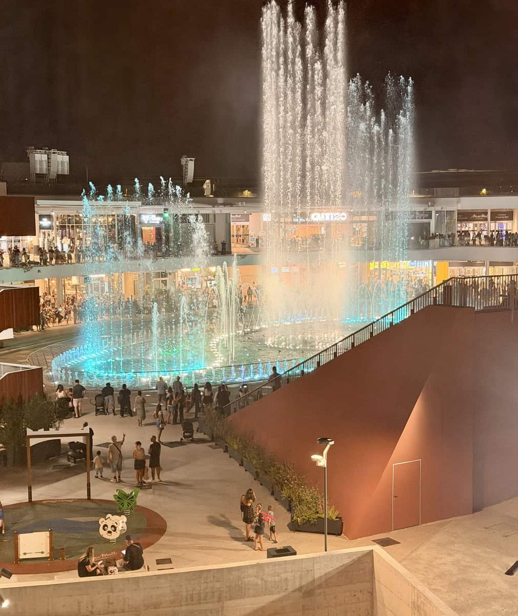 Night view of a lively shopping center with a large illuminated fountain display.