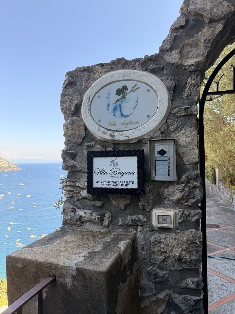 Villa Angelica sign on stone wall with sea view in background.